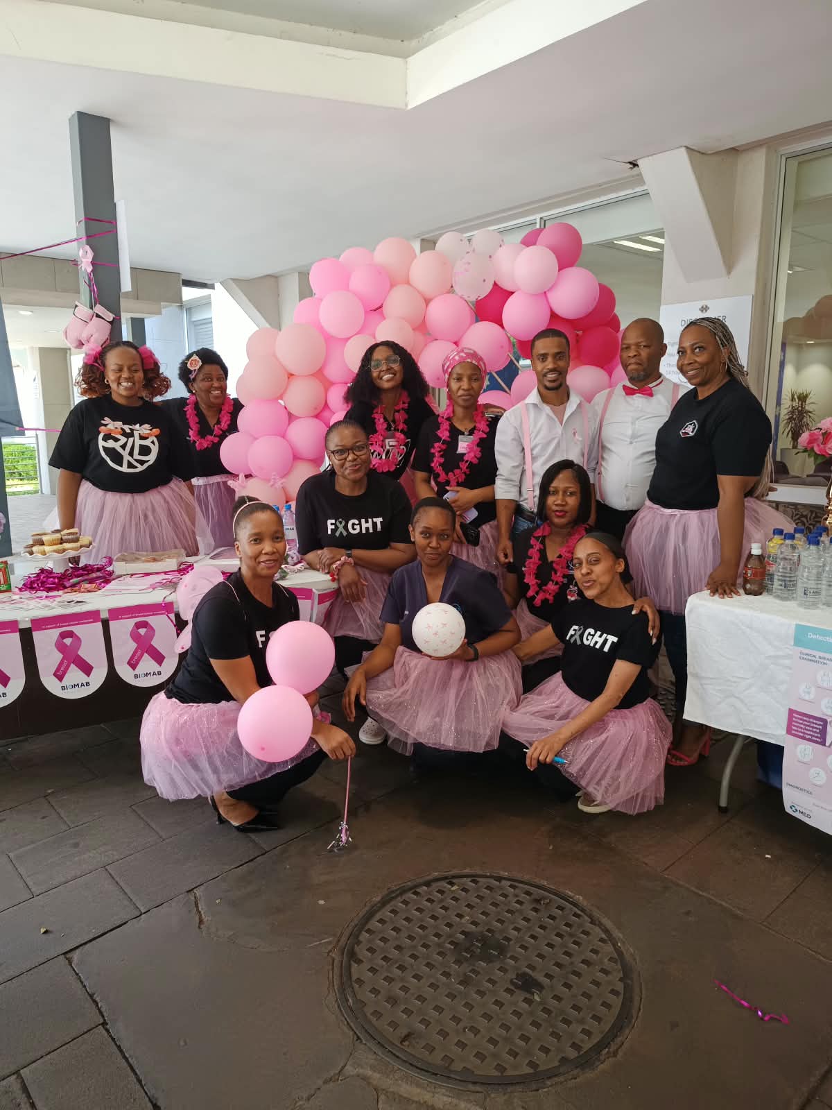 Garden City team gathered beside a breast cancer awareness display with pink balloons, ribbons and information materials